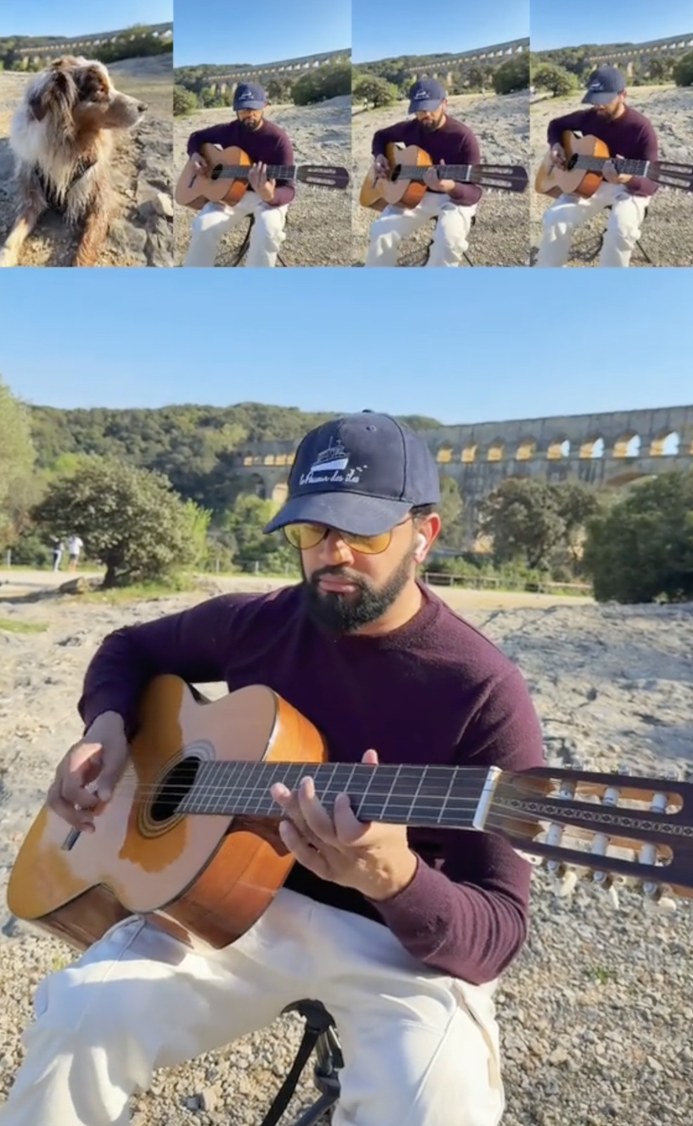 Playing guitar outdoors by ancient aqueduct. Lily-dog sits nearby. Clear sky, serene mood.